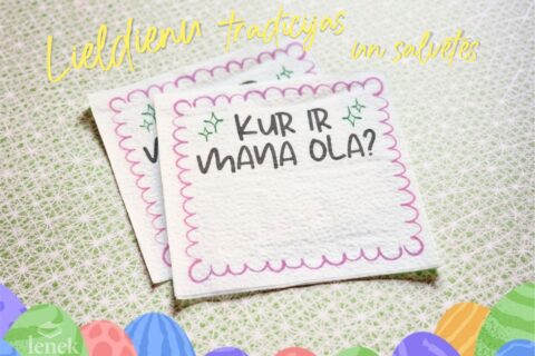 Easter-themed napkins with handwritten Latvian text placed on a light patterned background with colorful Easter eggs decoration. Easter-themed napkins with handwritten Latvian text placed on a light patterned background with colorful Easter eggs decoration